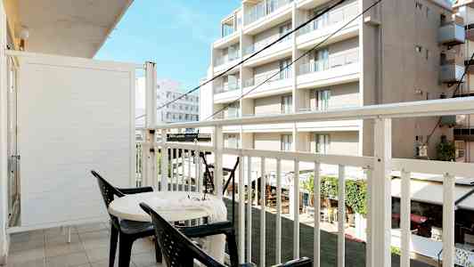 En balkong med två stolar och ett bord, utsikt mot byggnader. (AI-genererad text)