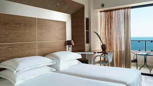 Hotellrum med två enkelsängar, skrivbord och utsikt över havet. (AI-genererad text)