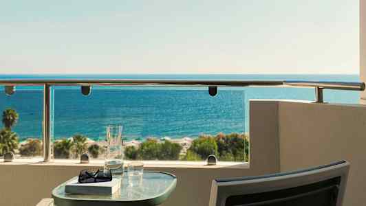 Utsikt över havet från en balkong med ett bord som har glas och bok placerade på. (AI-genererad text)