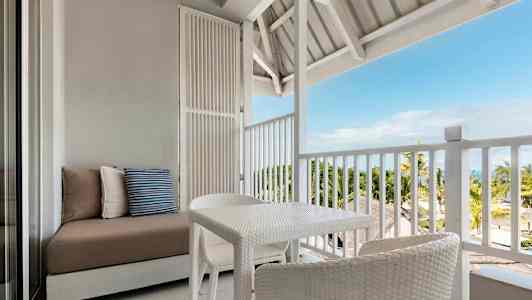 Möbler på en öppen balkong med vy mot palmer och hav. (AI-genererad text)