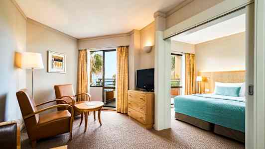 Ett hotellrum med sittgrupp, TV och säng med blå överkast. (AI-genererad text)