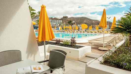 Terrass med möbler och utsikt över poolområde med gula parasoller. (AI-genererad text)