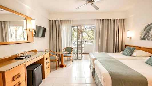 Hotellrum med två sängar, ett skrivbord, en platt-TV och en balkong med utsikt. (AI-genererad text)