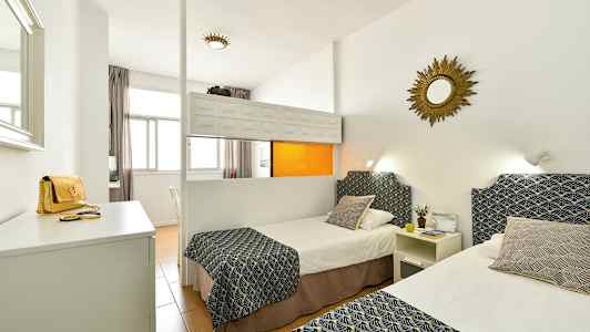 Ett hotellrum med två enkelsängar dekorerade med mönstrade överkast och kuddar, vita väggar och en spegel på väggen. (AI-genererad text)