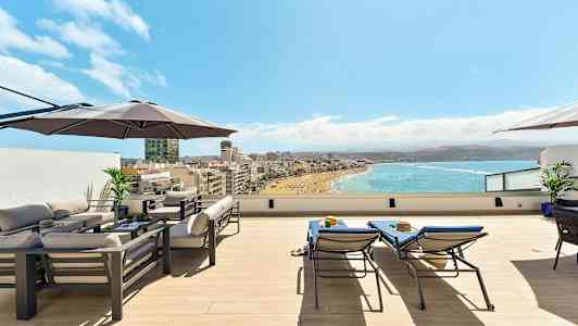 Tak terrass med möbler, parasoll och utsikt över en strand och hav. (AI-genererad text)