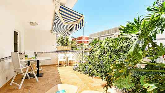 En terrass med utemöbler, markis och gröna växter i bakgrunden. (AI-genererad text)