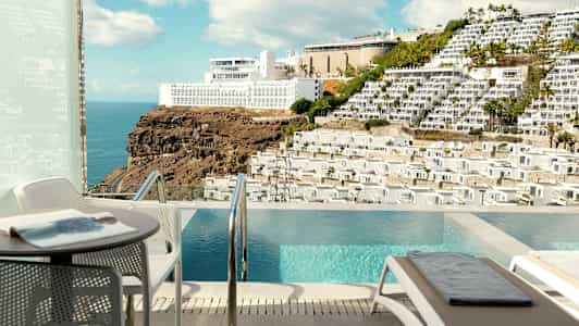 Utsikt från en uteplats med pool mot ett berg med byggnader. (AI-genererad text)