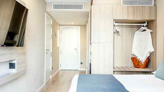 Ett hotellrum med en säng, ett väggmonterat TV och en garderob. (AI-genererad text)