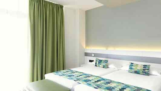 Ett hotellrum med två enkelsängar, gröna gardiner och matchande sängdekorationer. (AI-genererad text)