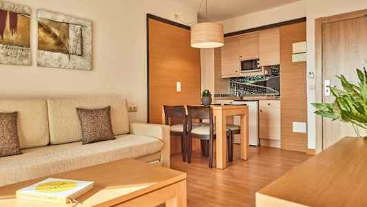 Foto av ett modernt hotellrum med en ljus soffa, ett träbord med stolar och ett hörnkök. (AI-genererad text)