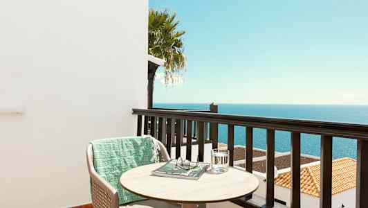 Utsikt från en balkong över havet med en stol, ett bord och en grön filt. (AI-genererad text)