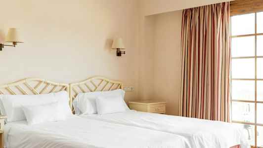 Två enkelsängar med vita sängkläder i ett hotellrum. (AI-genererad text)