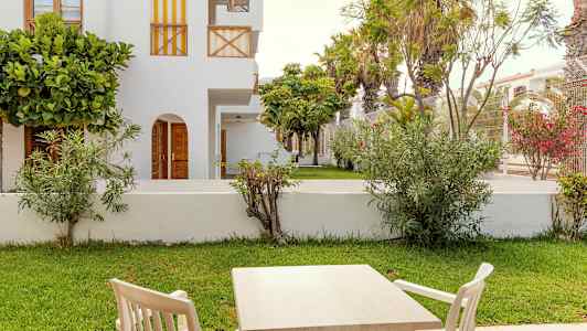 Utemöbler med bord och stolar framför en grön gräsmatta och vita byggnader. (AI-genererad text)