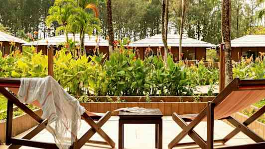 Två solstolar med en liten bord mellan dem, placerade på en uteplats med utsikt över en tropisk trädgård. (AI-genererad text)