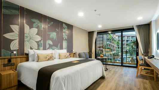 Hotellrum med en stor dubbelsäng, modern inredning och en balkong med utsikt över en pool och byggnader. (AI-genererad text)