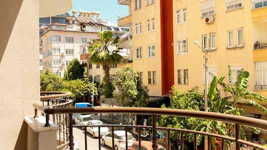 Utsikt från en balkong mot en gata omgiven av byggnader och grönska. (AI-genererad text)