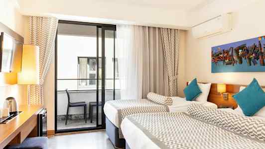 Ett hotellrum med två enkelsängar, en balkong med möbler och ett skrivbord med lampa och vattenkokare. (AI-genererad text)