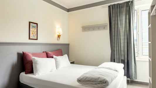 Bild på ett hotellrum med en dubbelsäng, dekorerad med sängkläder i vitt och rött samt en ljusgrå sänggavel. (AI-genererad text)