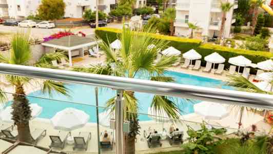 Vy från balkongen med en pool, parasoller och solstolar omgivna av växter. (AI-genererad text)