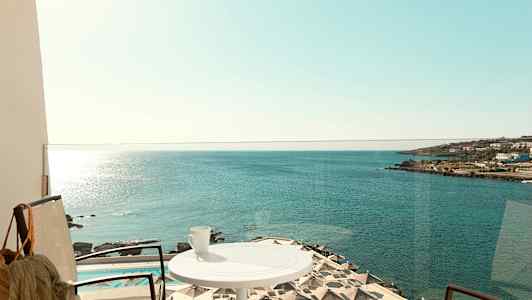 En balkong med utsikt över havet, parasoll vid en pool, och en kopp på ett bord. (AI-genererad text)