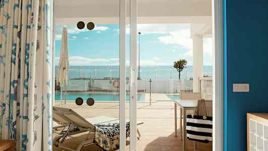 Bild av en solstol och en pool, sedd från en terrass genom glasdörrar. (AI-genererad text)