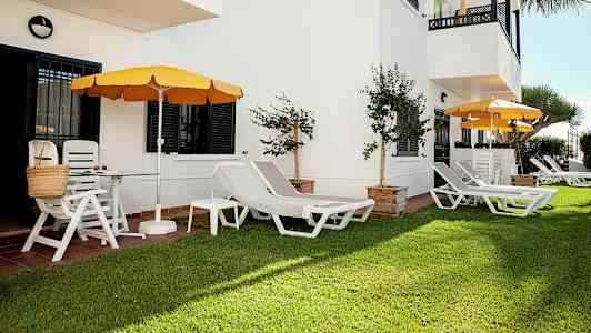 Grönyta med solstolar och parasoller vid en vit byggnad. (AI-genererad text)