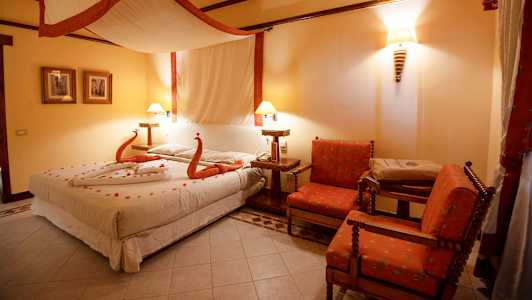 Ett sovrum med en säng dekorerad med handdukar formade som svanar och kronblad, två röda fåtöljer och varm belysning. (AI-genererad text)