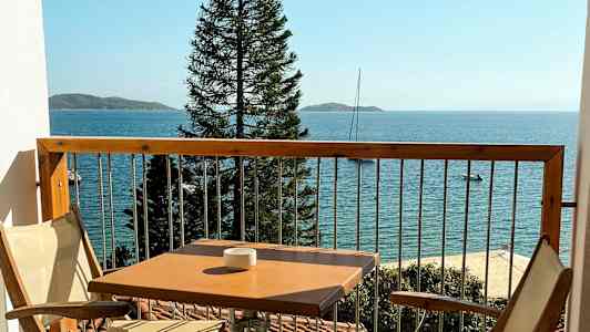 En balkong med två stolar och ett bord, havet och en mast syns i bakgrunden. (AI-genererad text)