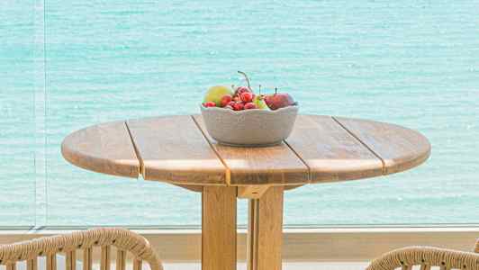 En träbord med stolar, en skål med frukt och utsikt över havet. (AI-genererad text)