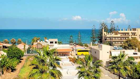 Utsikt över ett bostadsområde med palmer och byggnader, och havet synligt i bakgrunden under en klar blå himmel. (AI-genererad text)