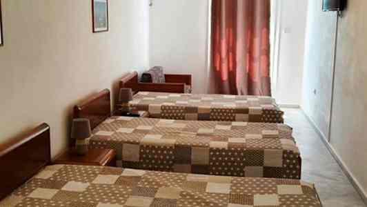 Tre enkelsängar i ett hotellrum med brunmönstrade överkast, luftkonditionering och en TV på väggen. (AI-genererad text)