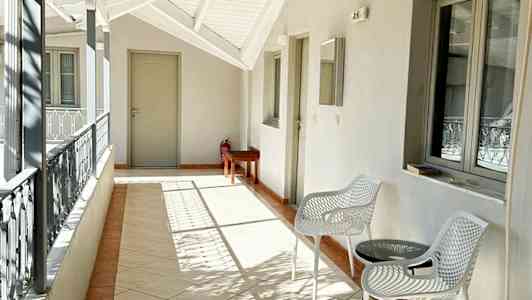 En öppen balkong med vita möbler, ett bord och en luftkonditioneringsenhet på väggen. (AI-genererad text)