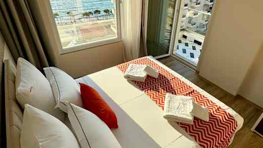 Ett hotellrum med en säng, fönster med utsikt över havet och handdukar på sängen. (AI-genererad text)