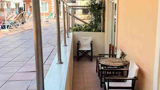 En uteplats med bord och stolar vid en gångväg nära en poolområde. (AI-genererad text)