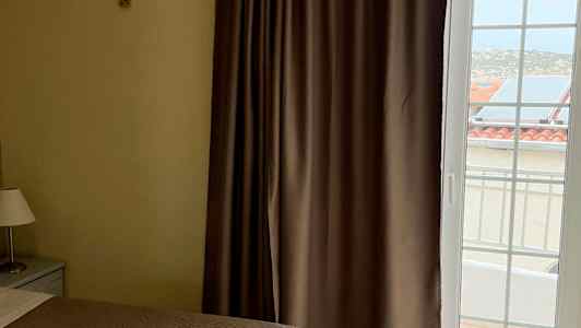 Två sängar med bruna överkast, ett fönster med gardiner och utsikt mot byggnader utanför. (AI-genererad text)