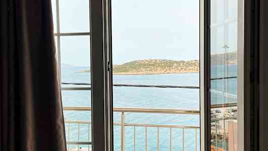 Utsikt från ett öppet fönster med en balkong, havet och en ö i bakgrunden. (AI-genererad text)