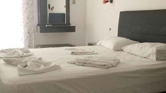 Ett sovrum med en dubbelsäng, sängkläder skymt på sängen. En spegel hänger på väggen bredvid. (AI-genererad text)