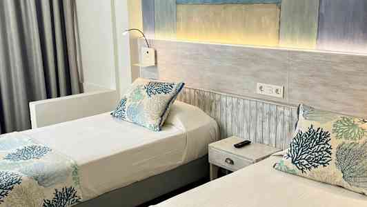 Två enkelsängar med blå och vita korallmönstrade sängkläder i ett hotellrum. (AI-genererad text)