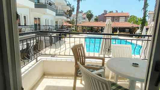 Utsikt från en balkong över ett poolområde och anslutande byggnader. (AI-genererad text)