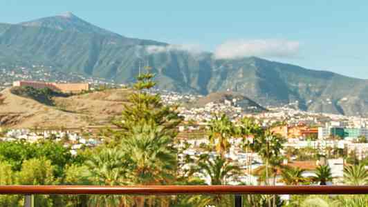 En balkong med bord där mat och dryck är serverad, utsikt över en stad med berg i bakgrunden. (AI-genererad text)