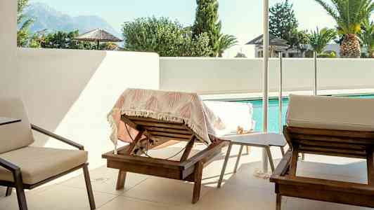 Bild på en terrass med solstolar, parasoll och pool i bakgrunden. (AI-genererad text)