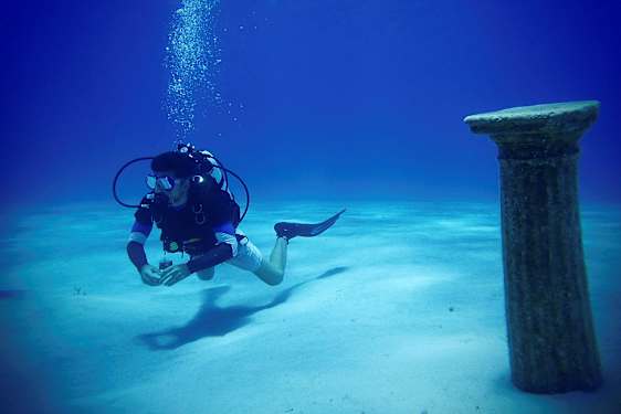 En dykare under vatten nära en antik pelare på havsbotten. (AI-genererad text)