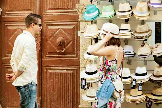 En person provar en hatt vid ett försäljningsbord med olika hattar. (AI-genererad text)