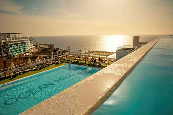 Utomhuspool med solstolar och utsikt över havet vid solnedgång. (AI-genererad text)