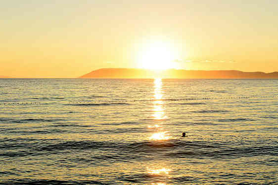 Solnedgång över havet med en siluett av en simmande person. (AI-genererad text)