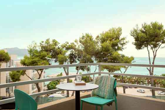 Utsikt från en balkong med ett bord och stol, utöver träd och hav. (AI-genererad text)