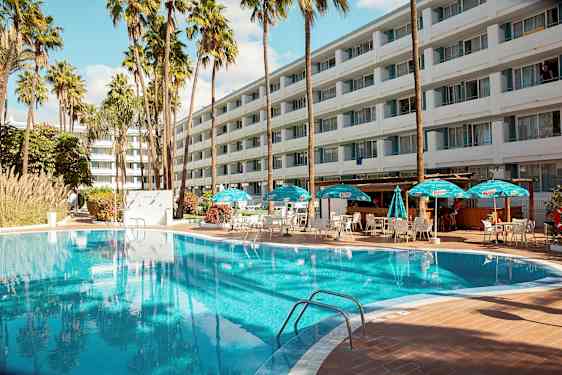 Utomhuspool med solstolar och parasoller framför ett stort hotell. (AI-genererad text)