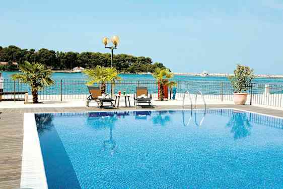 En pool med klarblått vatten och två solstolar bredvid. Havet syns i bakgrunden. (AI-genererad text)