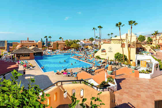 Ett hotellområde med en stor pool omgiven av solstolar och byggnader. (AI-genererad text)