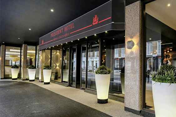 Ingången till President Hotel med stora vita krukor fyllda med grönska. (AI-genererad text)